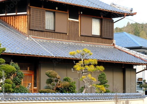 伝統的な日本家屋の瓦屋根と雨戸・手入れされた松の木と塀・田舎の立派な木造建築の風景・青空に映える和風住宅の外観