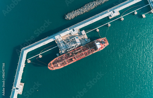 Aerial top down view of a large oil tanker docked at a pier in the port in process of loading.