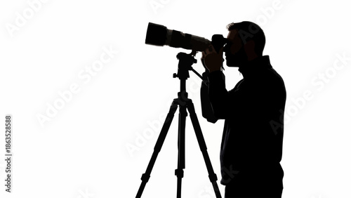 Silhouette of a man taking a photograph with a large lens camera on a tripod.