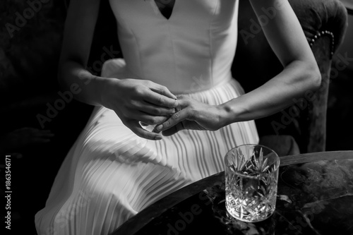 Canvas Print Bride in an elegant wedding dress gently holding her wedding ring beside a crystal glass on a marble table, artistic black and white moment symbolizing anticipation, love, and luxury