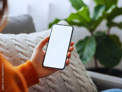 young black african woman holding smartphone in hand with white black empty mockup screen template using cell phone relaxing on sofa at home over shoulder view mobile apps advertising concept no logo