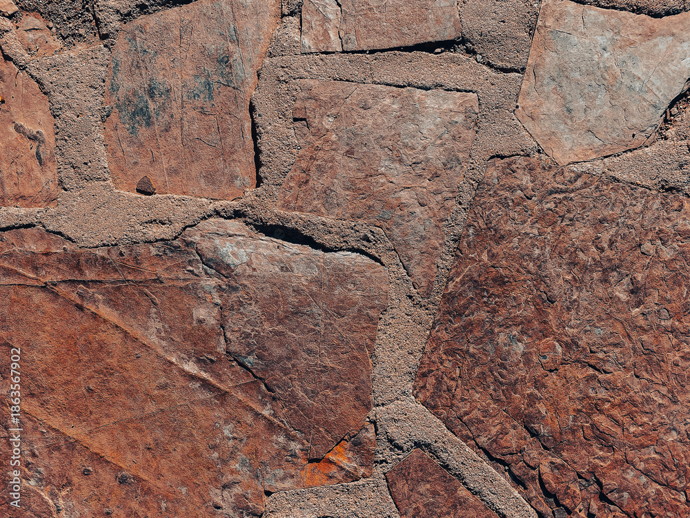 Fototapeta premium Large jagged stones are joined together with rough mortar creating a textured surface of reddish and earthy tones that looks weathered and solid with visible cracks