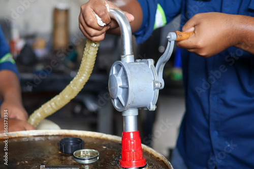 Manual rotary barrel pump installed on a red industrial oil drum being operated by a technician in a workshop facility.