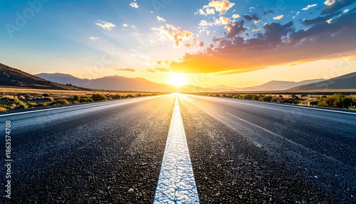 A wide road stretches into the horizon under a colorful sunset, with mountains in the background