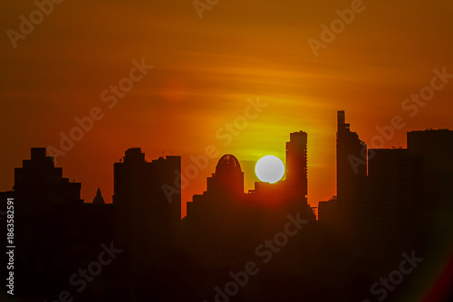 Stunning city skyline silhouette at sunset, with sun setting behind tall buildings, casting warm orange glow across sky. scene evokes sense of tranquility and urban beauty