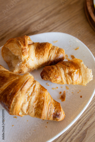 Fresh croissants arranged on a white plate with crumbs, highlighting flaky layers, warm tones, and a cozy homemade breakfast mood in soft natural light