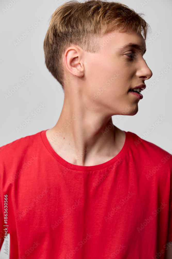 Naklejka premium Profile of a young male in a red shirt, side view against a neutral studio backdrop, highlighting casual fashion, clean lines and modern styling with soft lighting