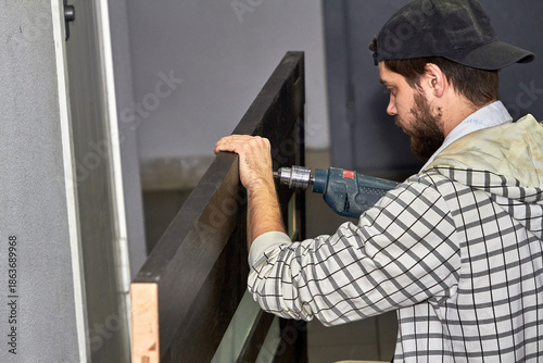 Male worker with screwdriver repairing door at home