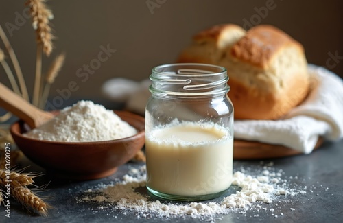 Flour in bowl next to jar with milk. Sourdough bread and wheat stalks in background. Preparing fresh dough for baking. Rustic kitchen scene.