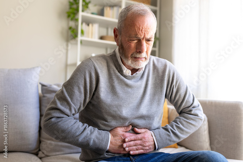 Photography Senior man suffering from abdominal pain while sitting on sofa at home
