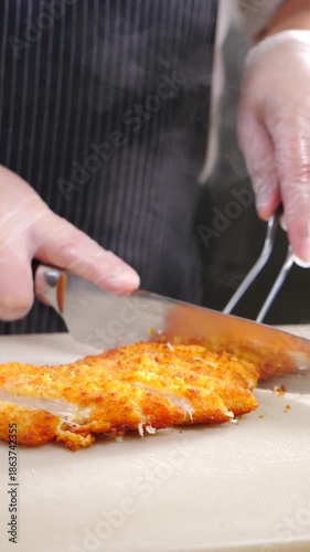 Crispy breaded cutlet or schnitzel being expertly sliced with sharp knife on white cutting board. Chef cutting delicious breaded schnitzel for salad. Vertical 4 k video