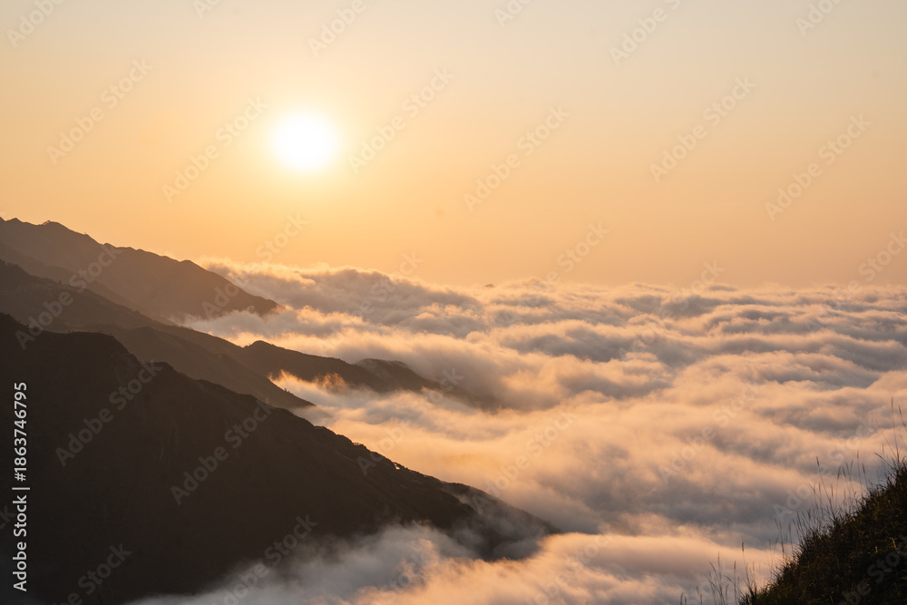 Fototapeta premium A golden sunset casts a glow over mountain peaks emerging from a sea of fluffy clouds