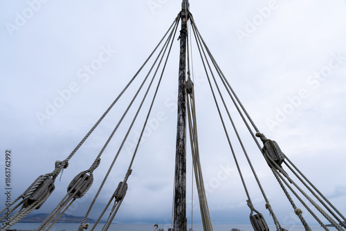 Vászonkép Low Angle View of Ship Mast and Intricate Rigging Ropes and Pulleys Against a Bright Overcast Sky, Emphasizing Nautical Structure and Tension