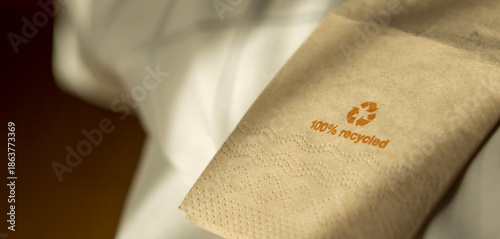 100% Recycled Paper Napkin. A close-up of a brown paper napkin with the text '100% recycled' and a recycling symbol printed in orange