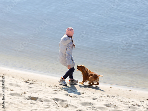 A girl walking a cocker spaniel dog on the beach near the water. Holidays at sea with pets. Joyful game with a dog near the river. Breeding thoroughbred hunting dogs. A place for swimming and relax