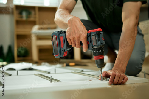 Fotografie Closeup man is working with furniture assembly using electric screwdriver