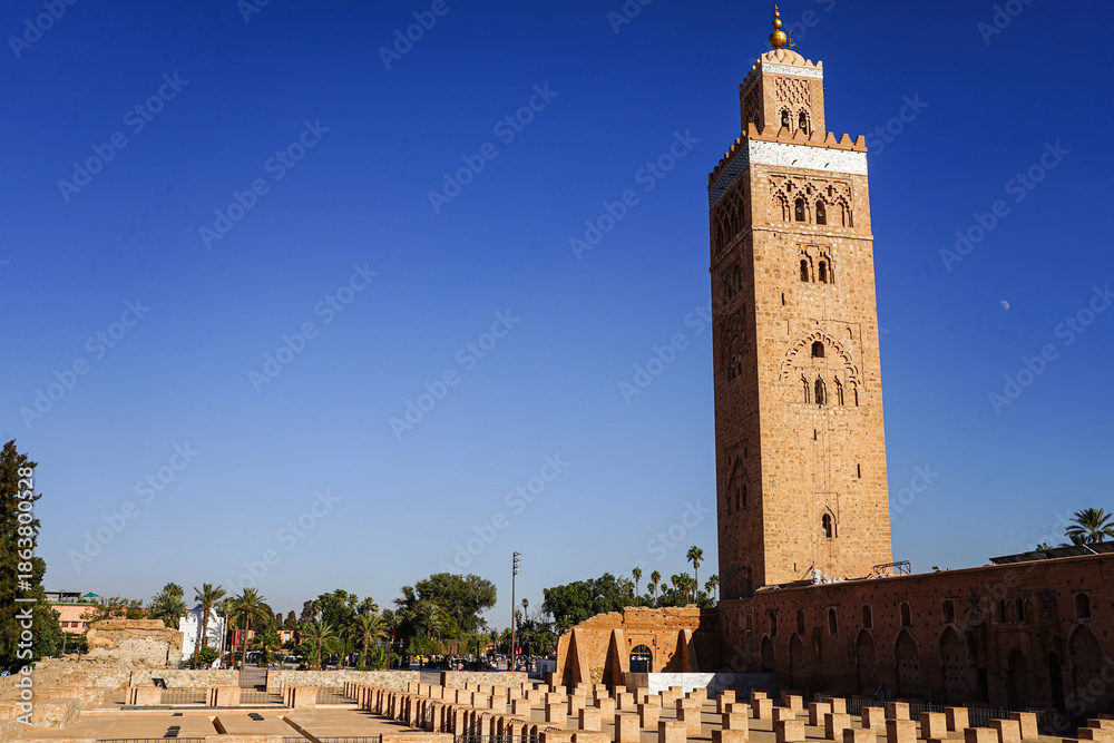 Fototapeta premium Koutoubia-Moschee in Marrakesch: Das markante Minarett aus rötlichem Sandstein erhebt sich vor tiefblauem Himmel über die historische Altstadt. 