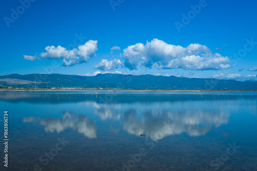 Foto White cumulus clouds are reflected on the calm blue surface of the Missolonghi salt marsh in western Greece
