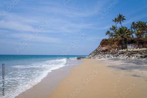 Fotografie Golden sand meets turquoise waves along Odayam Beach in Varkala, India, with palm trees crowning rocky cliffs under a clear blue sky