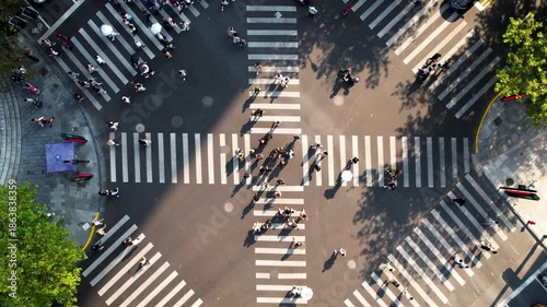 This is an aerial view of a city intersection. The zebra crossing is clearly visible in the picture. A large number of pedestrians are crossing the road through the zebra crossing. Some pedestrians ar