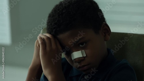 A young boy with a bandage on his nose, looking contemplative. He seems to be lost in thought Stock Video