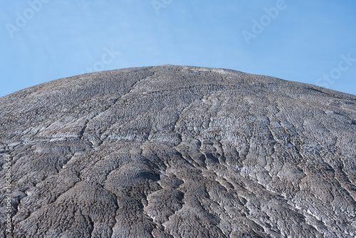 Canvastavla Detailed view of a massive, textured industrial slag heap, showcasing intricate erosion patterns against a clear blue sky
