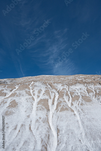Striking arid landscape featuring intricate white salt patterns on dry earth under a vast blue sky with wispy clouds. 