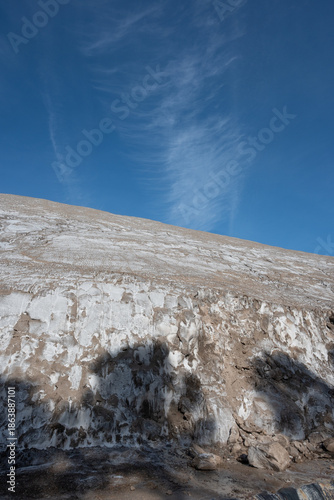 Striking arid landscape featuring intricate white salt patterns on dry earth under a vast blue sky with wispy clouds. 