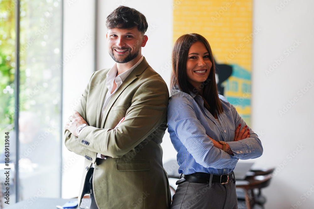 Fototapeta premium Business partners stand back to back in modern office setting during daytime while smiling and showing confidence in their professional attire