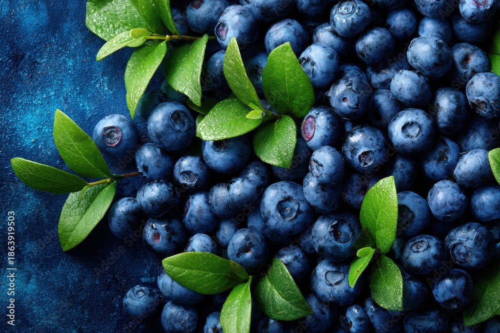 Obraz premium Close-up of fresh, ripe blueberries and green leaves on a dark blue textured background. Macro shot showcasing healthy antioxidants, freshness, and vibrant color.