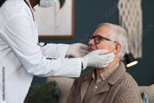 Принти на полотні Senior Caucasian man sitting while Black woman doctor wearing gloves examining h
