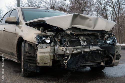 Принти на полотні Close-up of the front of a wrecked car after an accident with a badly deformed hood, broken headlights and a damaged radiator on the road