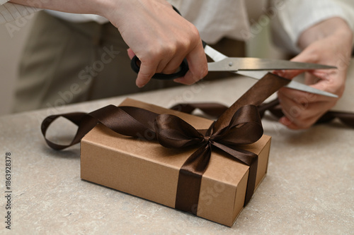A woman's hands wrap a gift in a box with a bow