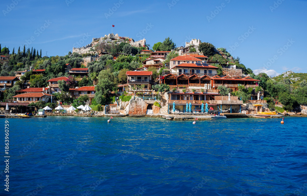 Fototapeta premium Picturesque Turkish coastal village with a striking white mosque featuring a green-topped minaret rising above terracotta-roofed houses along a serene waterfront.