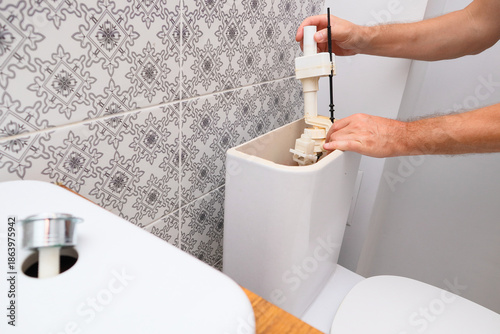 Plumber repairing or replacing the fill valve of a toilet flush tank.