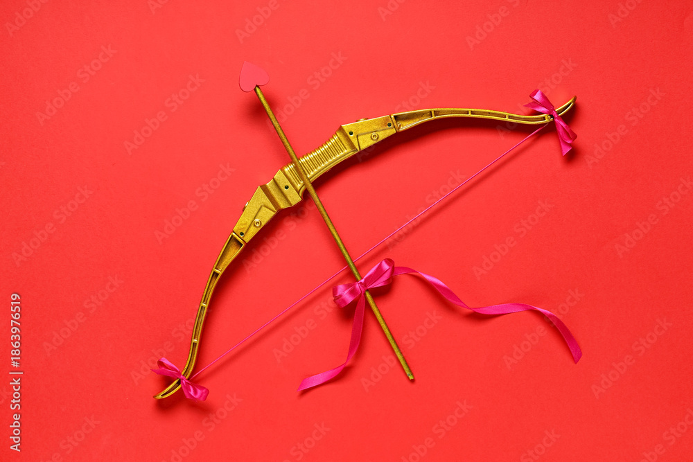 Obraz premium Golden cupid's bow on red background. Valentine's Day celebration