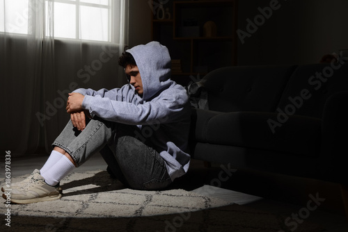Sad young man sitting in da...