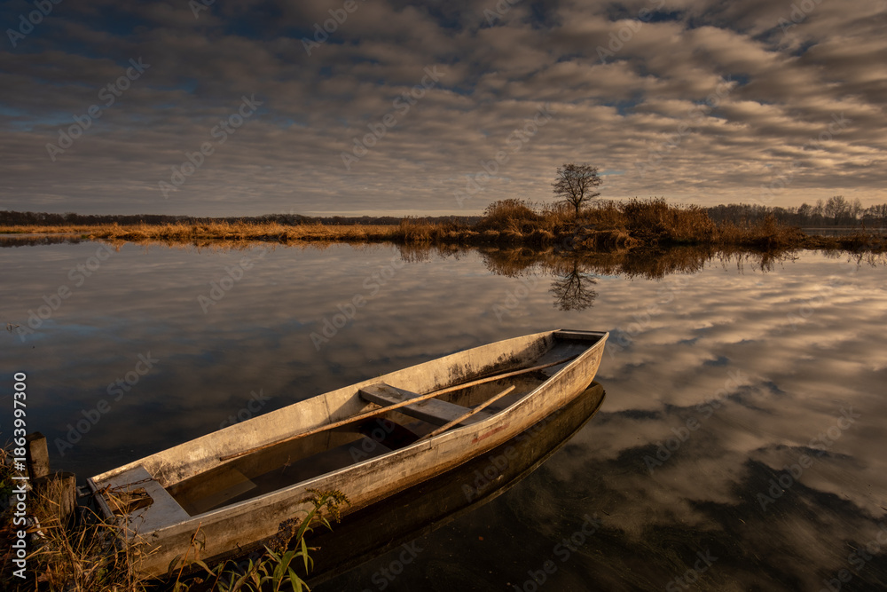 Obraz premium Abandoned wooden boat on calm lake with dramatic cloud reflections
