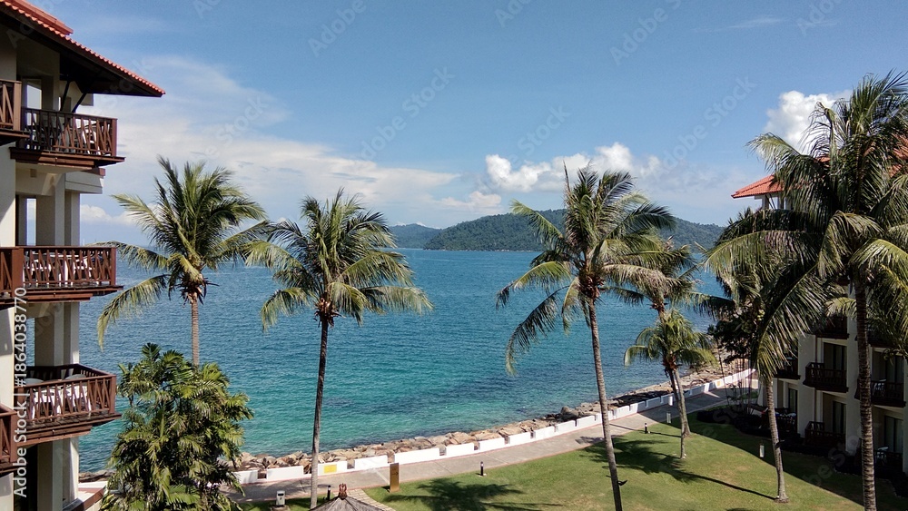 Fototapeta premium A scenic tropical beach view with palm trees, turquoise ocean water, and resort buildings along the shoreline.