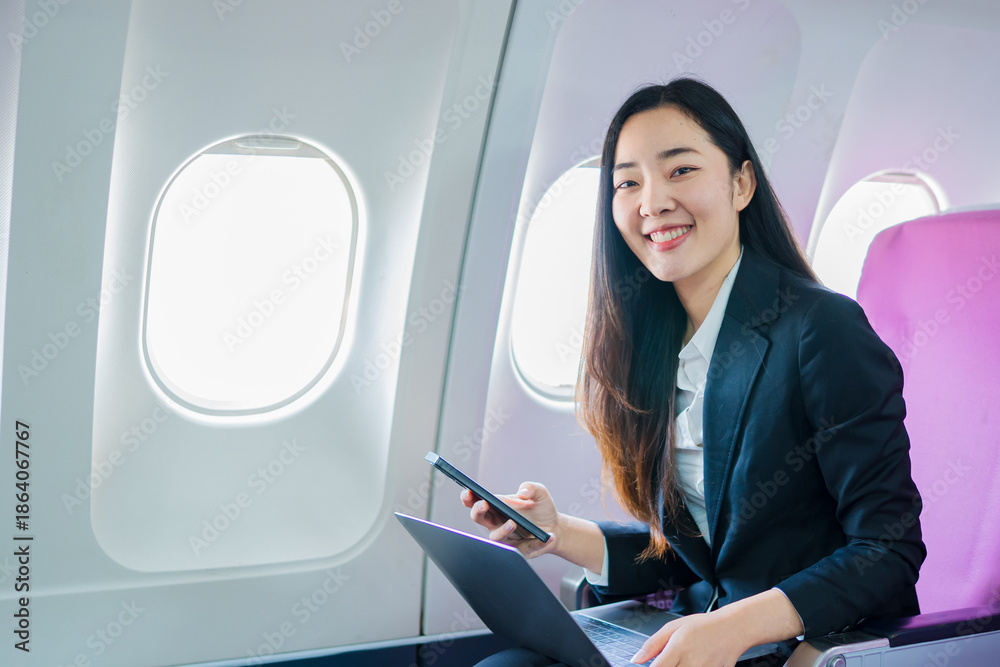 Fototapeta premium A woman is sitting on an airplane, working and looking at her laptop.