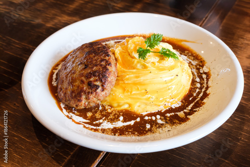 Omelette rice with Hamburger Steak in brown sauce (Omurice) served on a white plate
