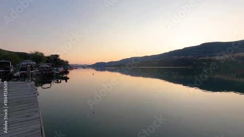 Breathtaking aerial footage capturing a serene river at sunrise or sunset, framed by majestic mountains and a colorful sky. The calm water mirrors the vibrant hues of the sky, creating a peaceful