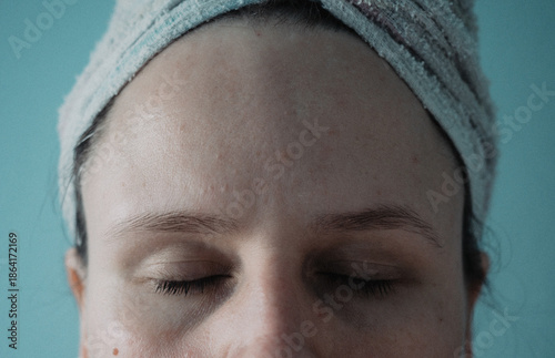 Closeup shot of woman with closed eyes wearing hair in towel wrap, bare skinned natural face of middle-aged femal with facial blemishes and big pores, smudged mascara, analog photo with film grain