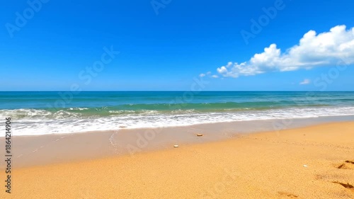 Ocean waves washing onto a sandy beach under a clear blue sky