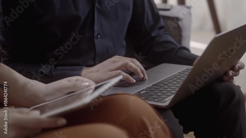 Close-up of colleagues working together using laptop and tablet in a modern office environment.