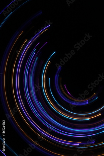 A long exposure photograph. Light painting photography; vibrant multicolour fairy lights in a circle swirl pattern against a black background