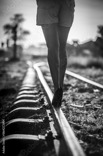 Woman walking on railway track balancing in high heels, concept of risk, uncertainly and life journey in black and white