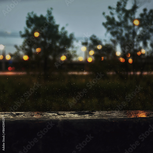 photo depicting rainy evening scenery, in the foreground raindrops, in the background blurred silhouettes of trees and lanterns