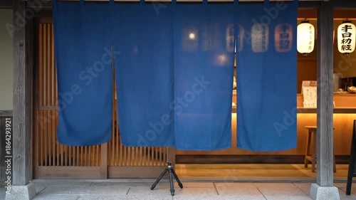 Traditional Japanese Noren Curtain Entrance to a Cozy Restaurant at Dusk Illuminated by Soft Lantern Light Featuring Wooden Architecture and Stone Pavement in Kyoto Japan