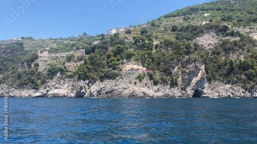 Yacht sailing along the Amalfi coastline exploring beautiful rock hills with hidden grottos and old scattered house among the nature, cruise along mediterranean coastline during summer vacation